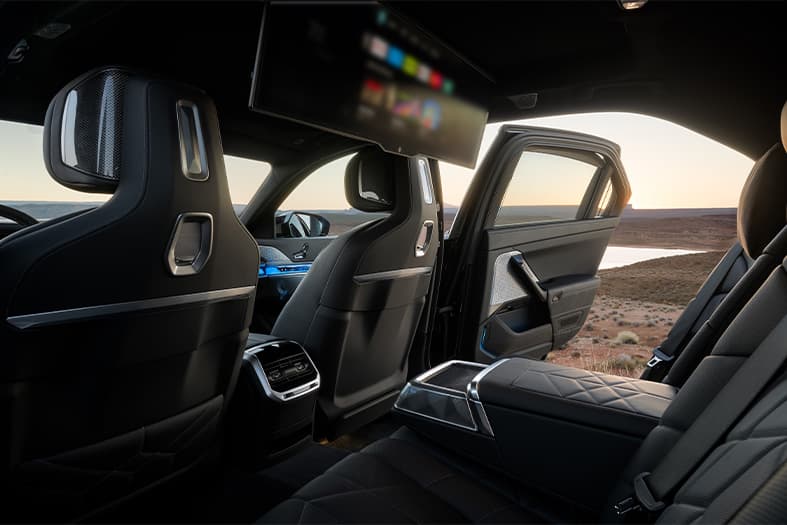 Backseat and theatre screen display of a 2026 BMW i7 M70 parked in flat, desert landscape with the sun setting in the background.