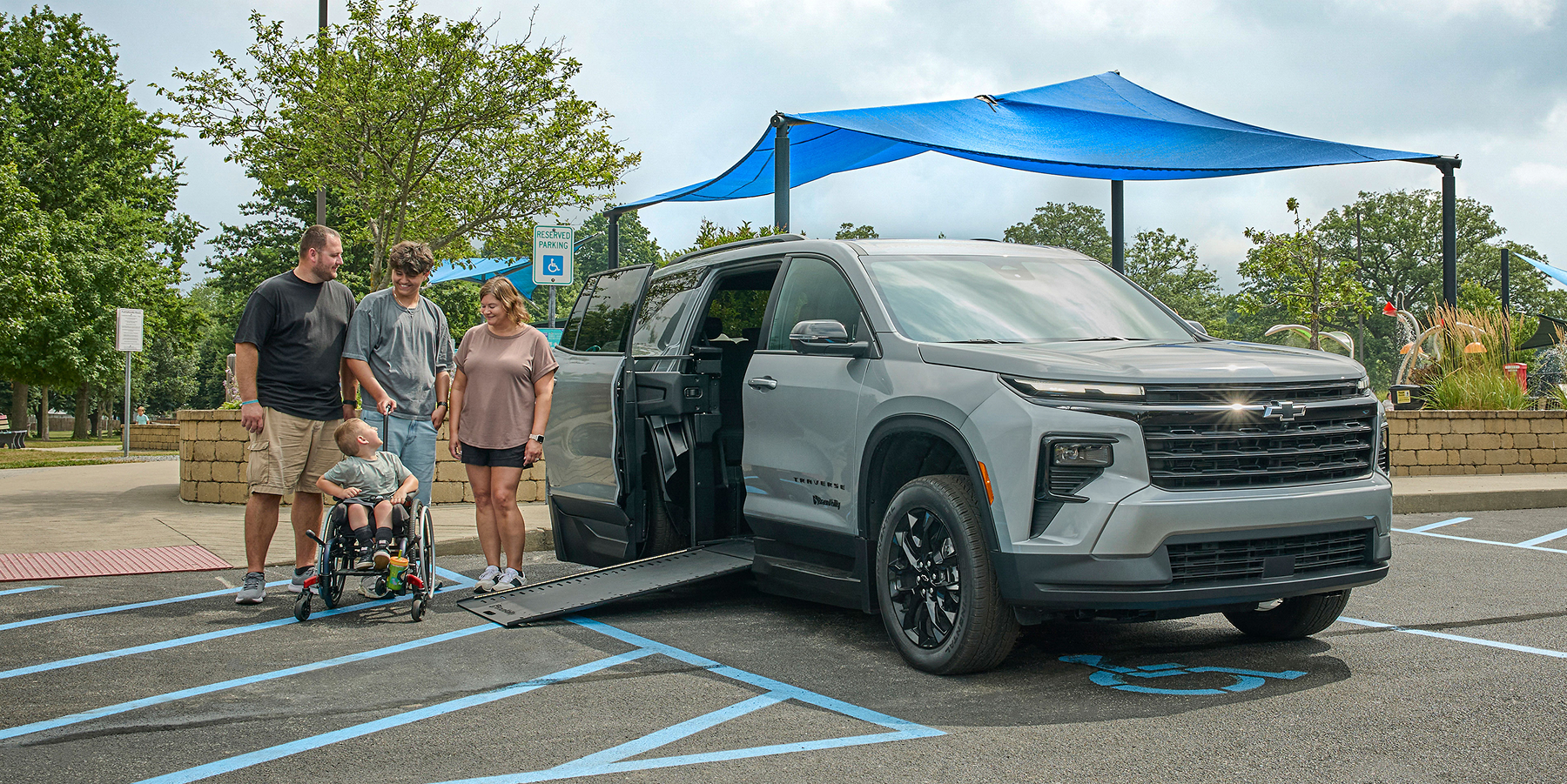 Family with child in wheelchair standing outside a parked Chevy Traverse with its side ramp down.