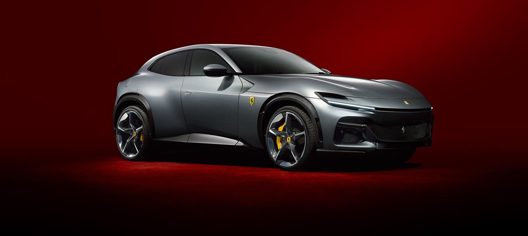 Matte gray Ferrari Purosangue SUV against a dramatic red background.
