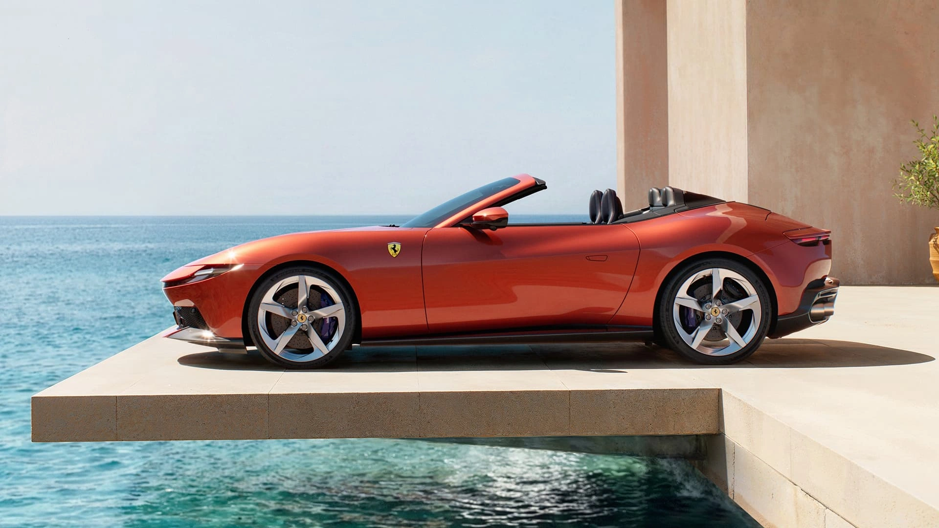 Ferrari Amalfi Spider in red, side profile view, parked on an elevated terrace overlooking the ocean