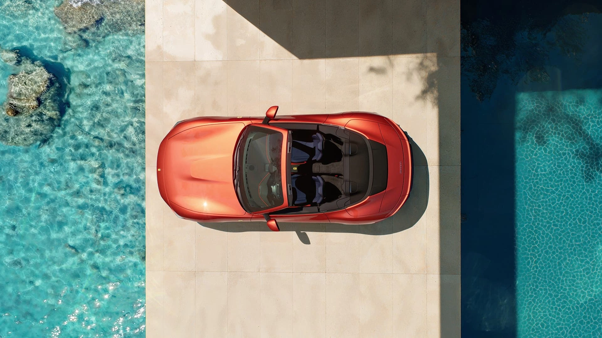 Ferrari Amalfi Spider in red, aerial top-down view, parked between ocean and pool