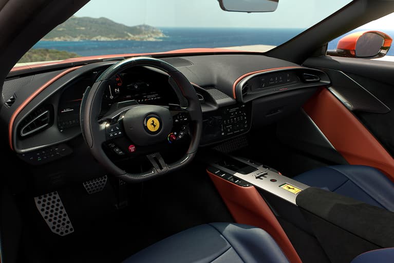 Ferrari interior with red and navy leather, steering wheel with prancing horse logo, and ocean view through the windshield
