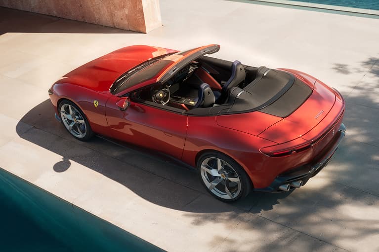 Red Ferrari convertible sports car with the top down, photographed from an aerial perspective on a sunlit concrete surface