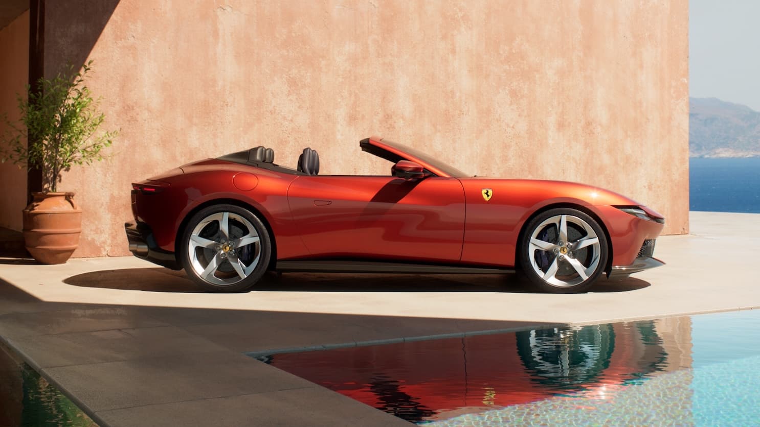 Ferrari Spider in red, side profile view, parked on a poolside terrace with coastal scenery.