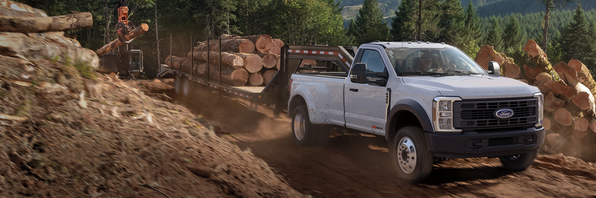 White Ford truck driving down a dirt road while hauling a trailer of logs