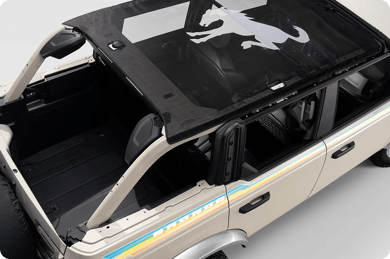 Aerial view of a white Ford Bronco with the top removed, showing a black soft top with the Bronco horse logo and retro side stripe graphics.