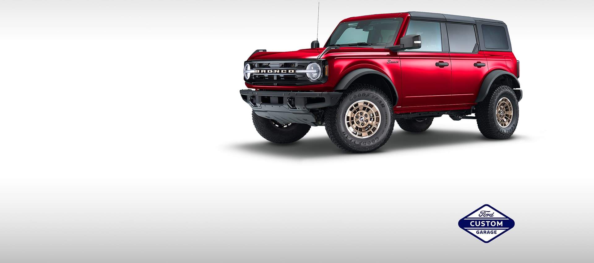 Red Ford Bronco with bronze wheels and off-road tires on a white background, featuring the Ford Custom Garage badge.