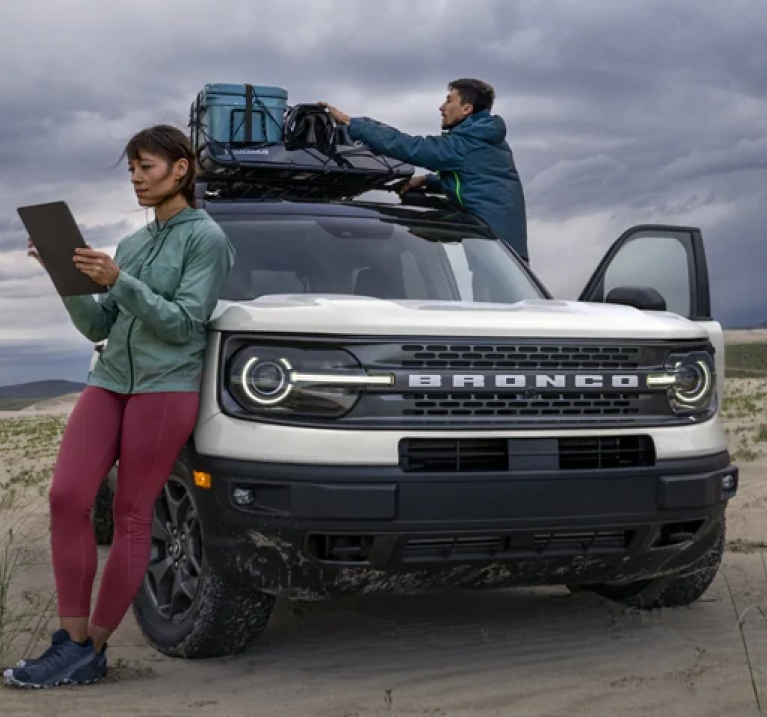 White Ford Bronco Sport with a person leaning against it while another unloads the roof rack