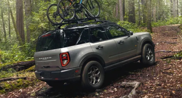 A grey Ford Bronco Sport driving through a forest with 2 bikes on the roof rack