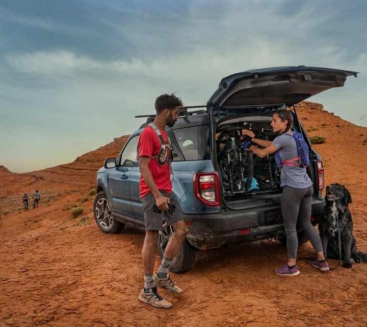 Woman removing bicycle from Ford Bronco Sport back door parked in orange colored hill