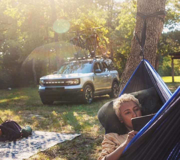 Ford Bronco Sport in background as woman reads book in hammock
