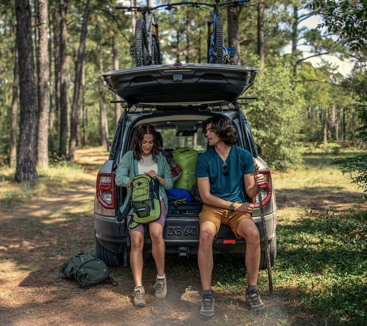 Woman and man sitting in the back of Ford Bronco Sport in the middle of the forest. 