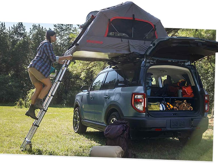 Woman climbing ladder to a tent pitched atop a 2025 Ford Bronco® Sport with rear door open