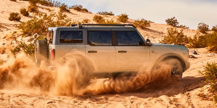 A side shot of a Gray Ford Bronco driving through the dessert.