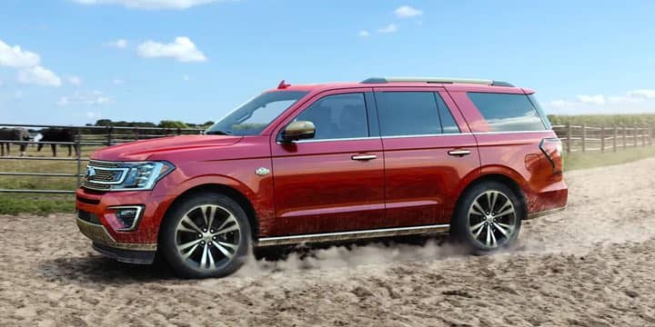 A side shot of a Red Ford Expedition driving on a ranch.