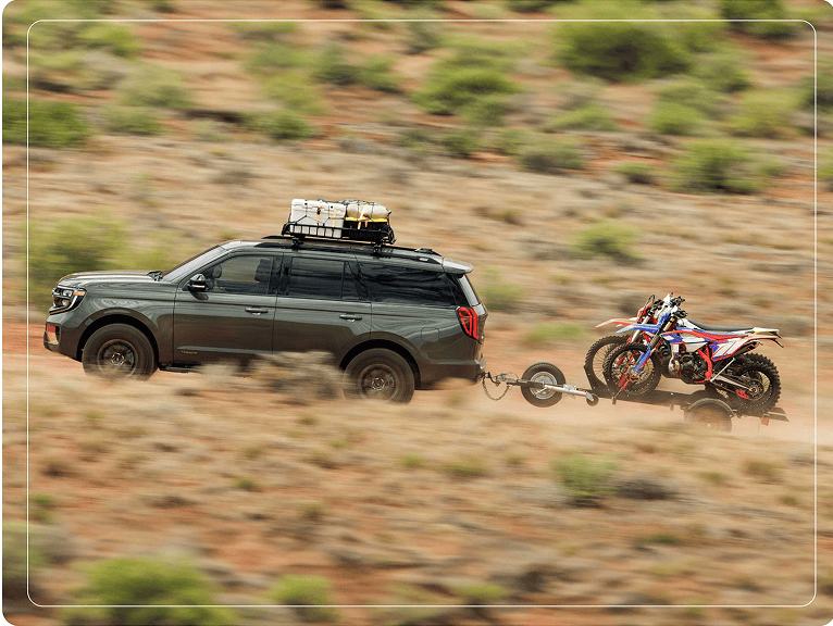2025 Ford Expedition® TREMOR® SUV with a driver towing a dirt bike trailer on a desert road