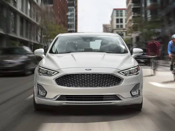 Front view of a white Ford Fusion Hybrid on a city street