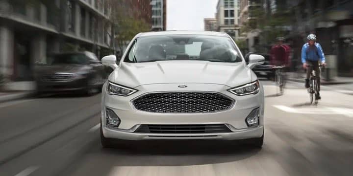 Front view of a white Ford Fusion Hybrid driving on the street