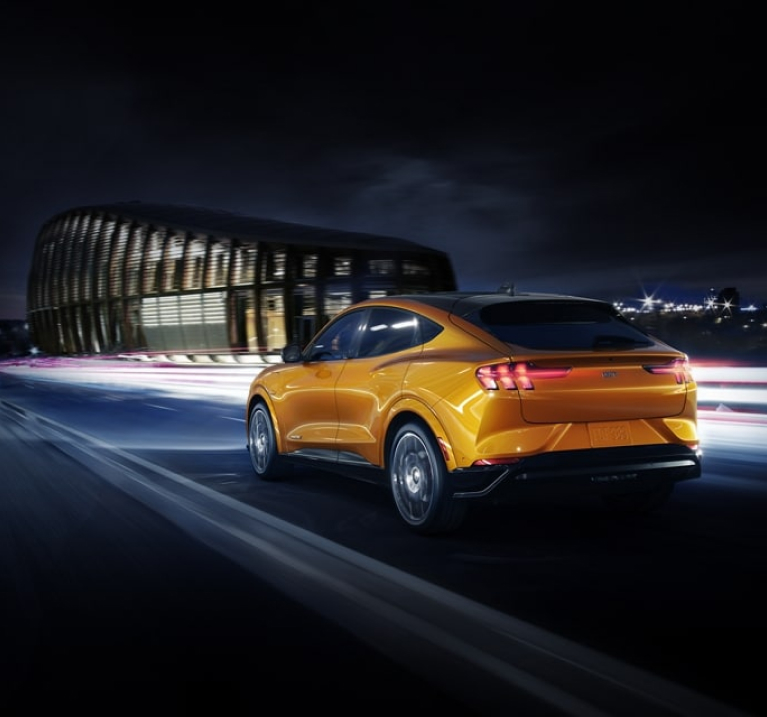 Yellow Mustang Mach-E driving at night under bridge.