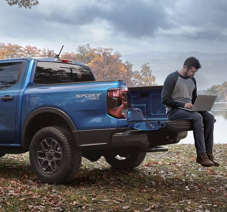 man sitting on the tailgate of a Ranger working on a laptop