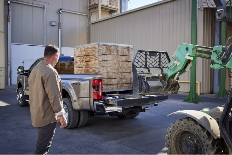 Man standing behind Super Duty waiting while tractor forklift loads bed