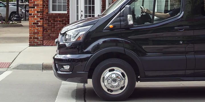 A side view of a Black Ford Transit van parked on a city street at an intersection.