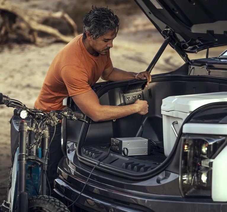 Man charging something inside the storage area of a ford f-150 lighting truck.