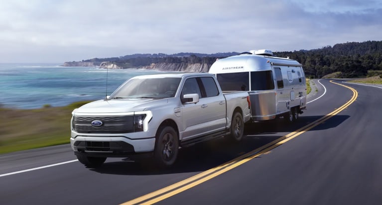 a ford f-150 lightning driving down coastal road towing a trailer.