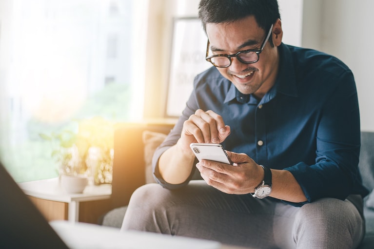Smiling person in glasses sits in a well-lit room and uses their smartphone to learn about Flex Buy financing. 