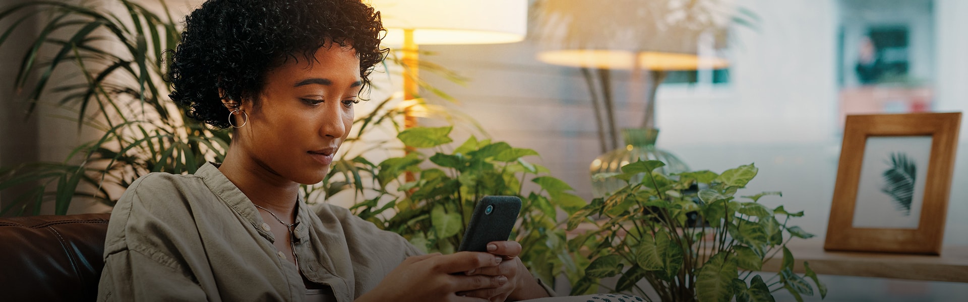 Person in a room with plants and soft lighting uses their phone to learn about Flex Buy financing.