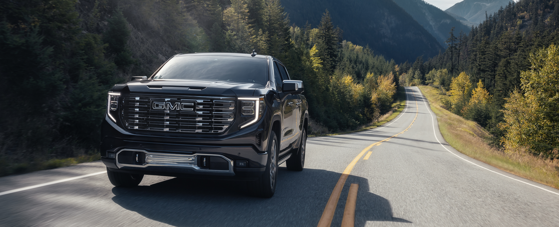 GMC truck driving down a forest road