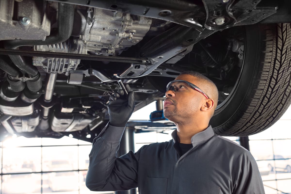 Service tech holding a flashlight, looking under chassis of vehicle.