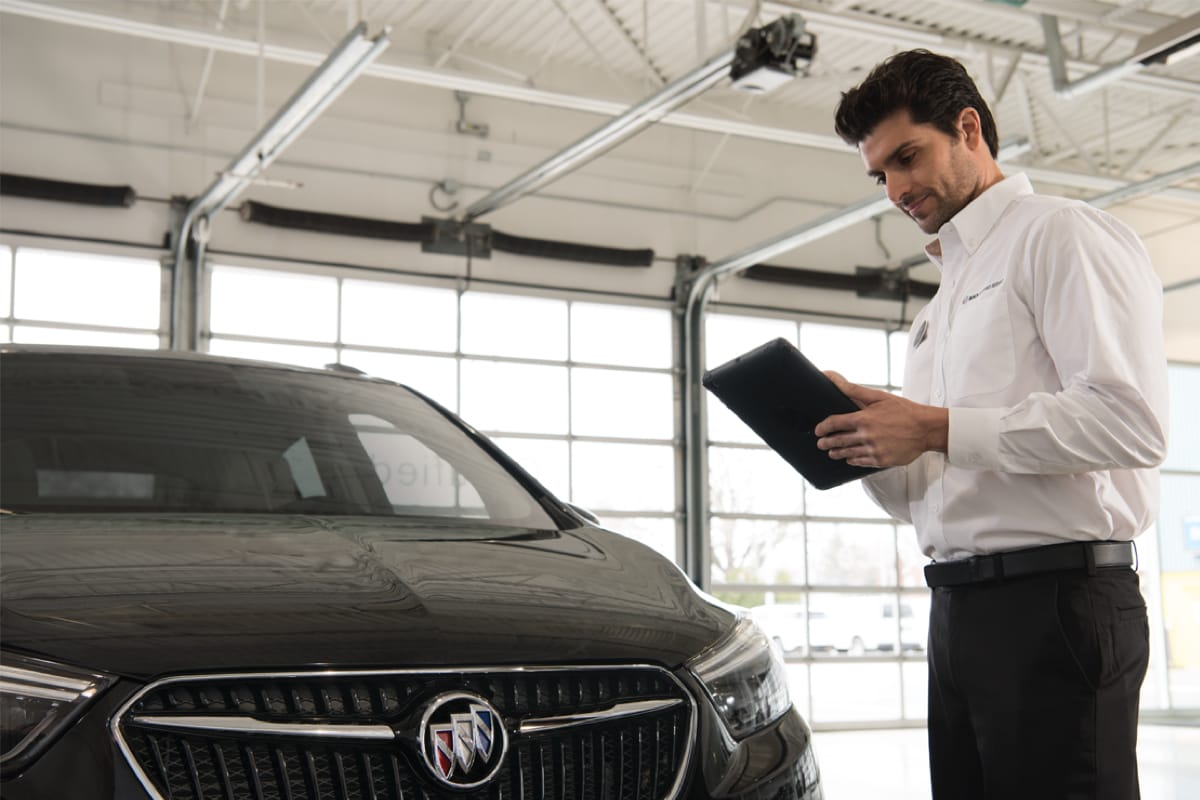 A sales guy looking at his ipad, while standing next to a Buick vehicle