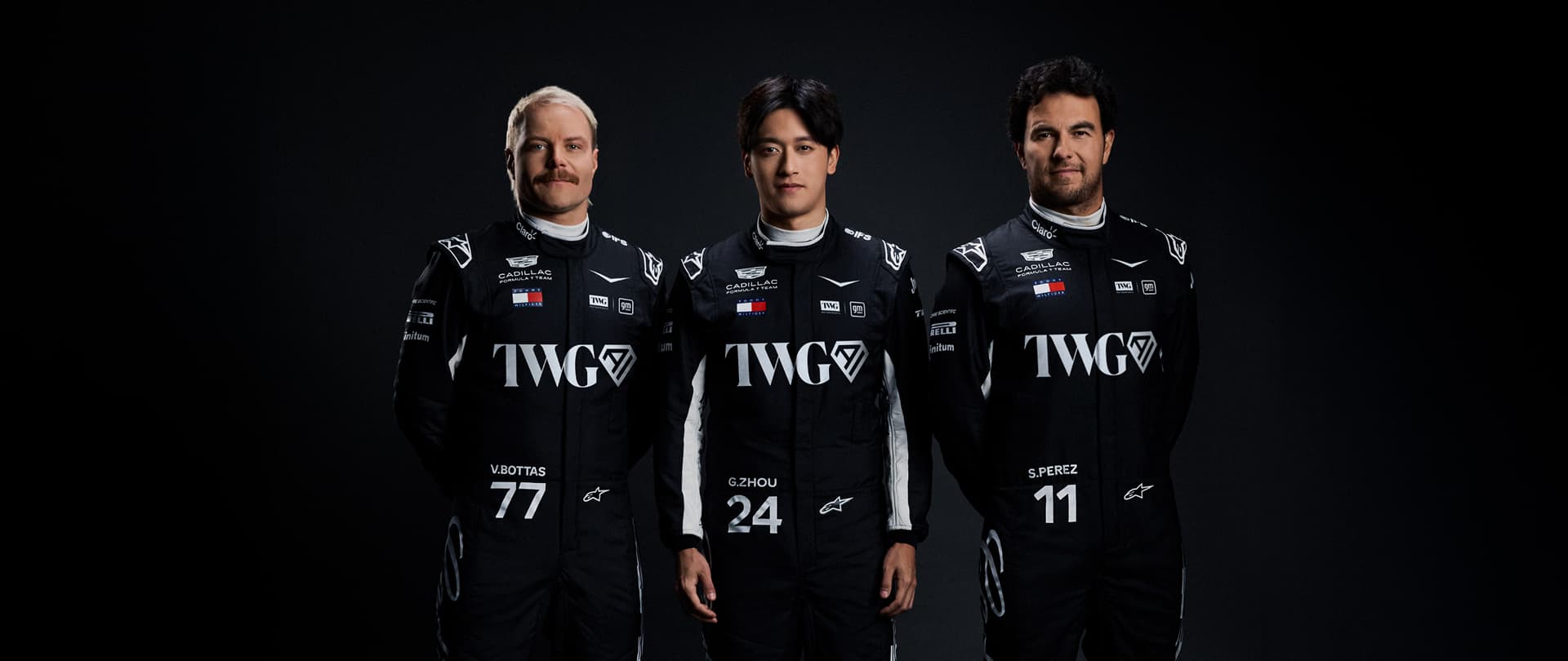 Three Team Members Wearing Matching Black Racing Suits With Cadillac And Sponsor Logos Stand Side By Side Against A Dark Studio Background.