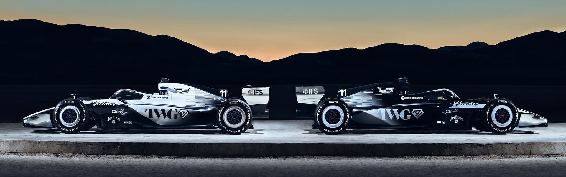 Two Cadillac Racing Cars Facing Outwards on a Circular Structure Outside in the Evening.