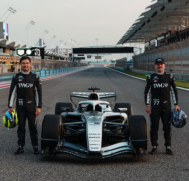 Two Cadillac F1 Team Drivers Posing Next to a Racecar Parked on the Track