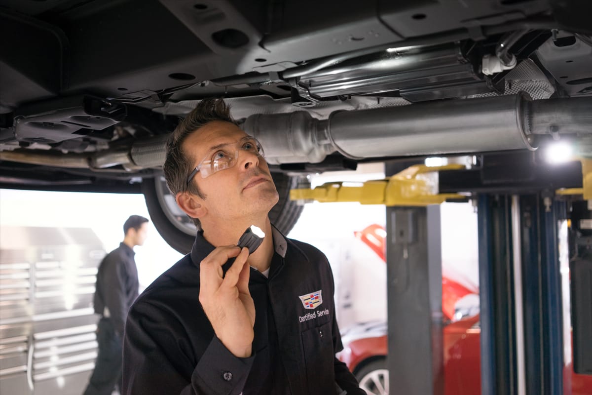 Service tech holding a flashlight, looking under chassis of vehicle.