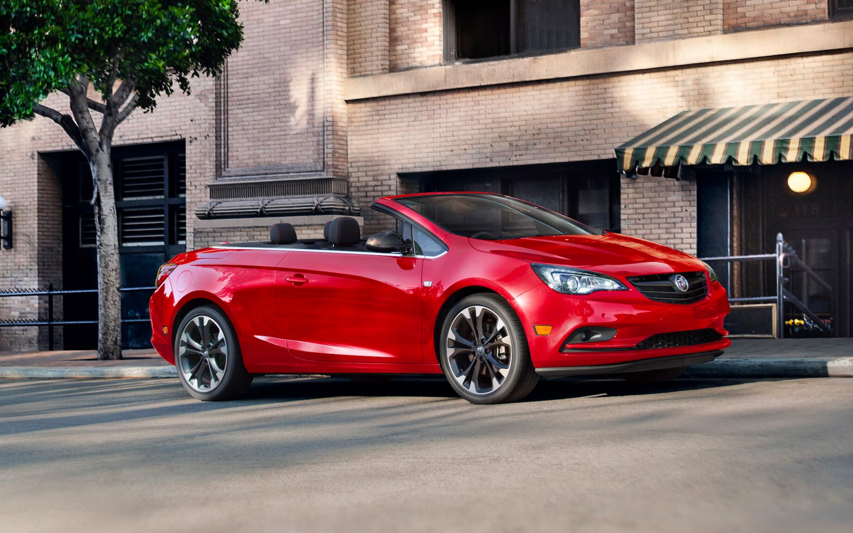 A red Cascada parked on the street, infront of a building.