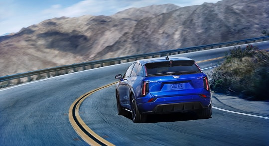 Rear View of a Blue 2026 OPTIQ-V Driving on a Curve of a Mountain Row