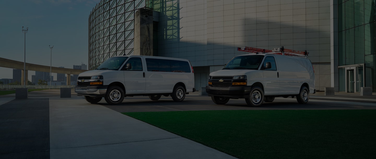 Two Chevrolet Vans parked in front of a modern building