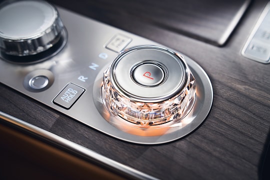 Interior close up of driver's hands on shift by wire gear selector wheel inside the Genesis G80