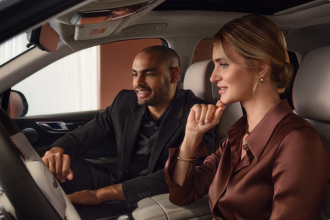 Interior view of a luxury genesis vehicle with two passengers exploring dashboard features