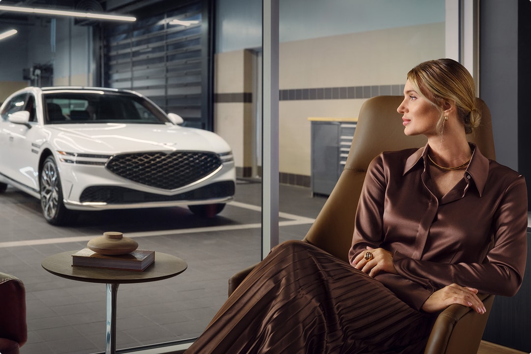 View of Genesis G90 in service center through glass, person seated in waiting area.