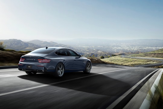 Genesis G80 in Ceres Blue driving on a winding road with motion blur