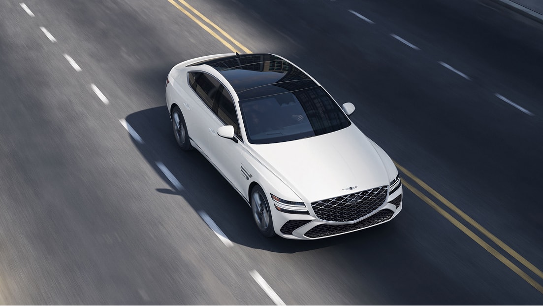 3/4 front passenger overhead view of Genesis G80 in white driving on two lane road