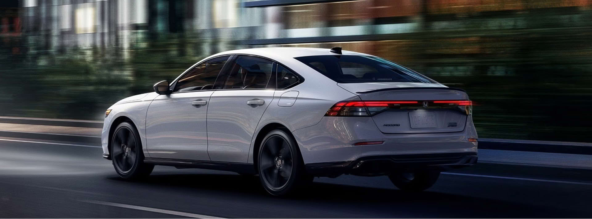 A white Honda accord hybrid driving down a road in autumn.
