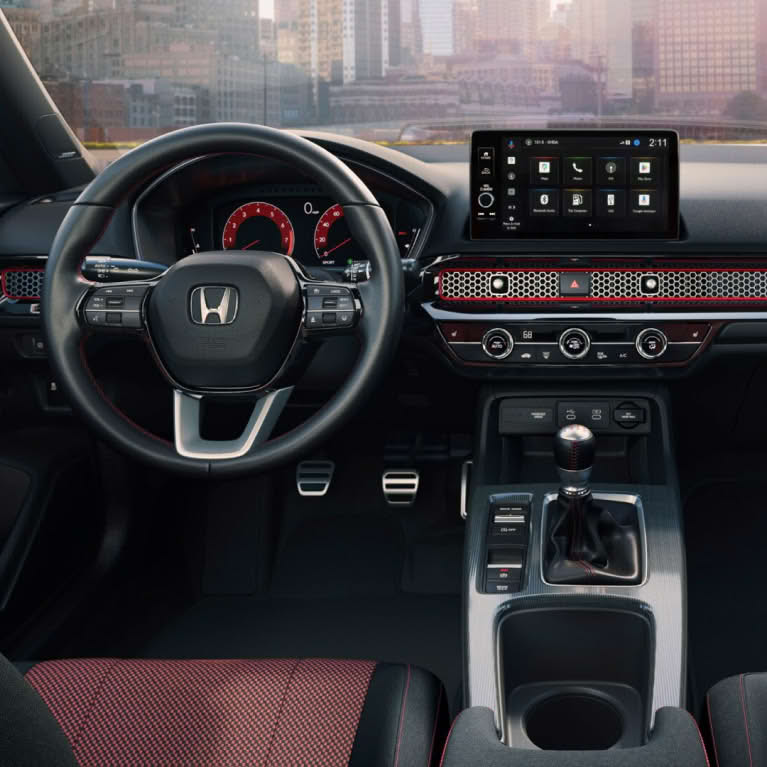 Civic Si steering wheel and dashboard with outside view of a city through windshield.