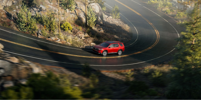 Wide shot of a red Honda Pilot driving on a curved mountain road