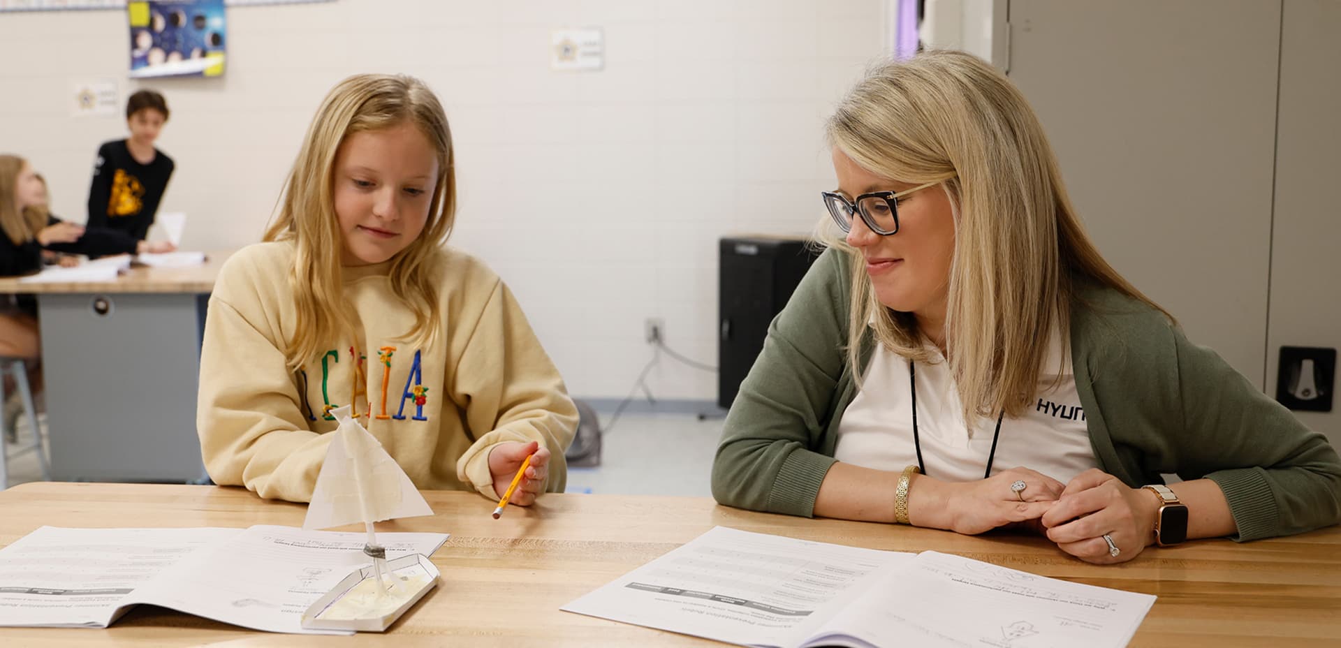 A Hyundai representative working one-on-one with a young student on a STEM activity in a classroom.