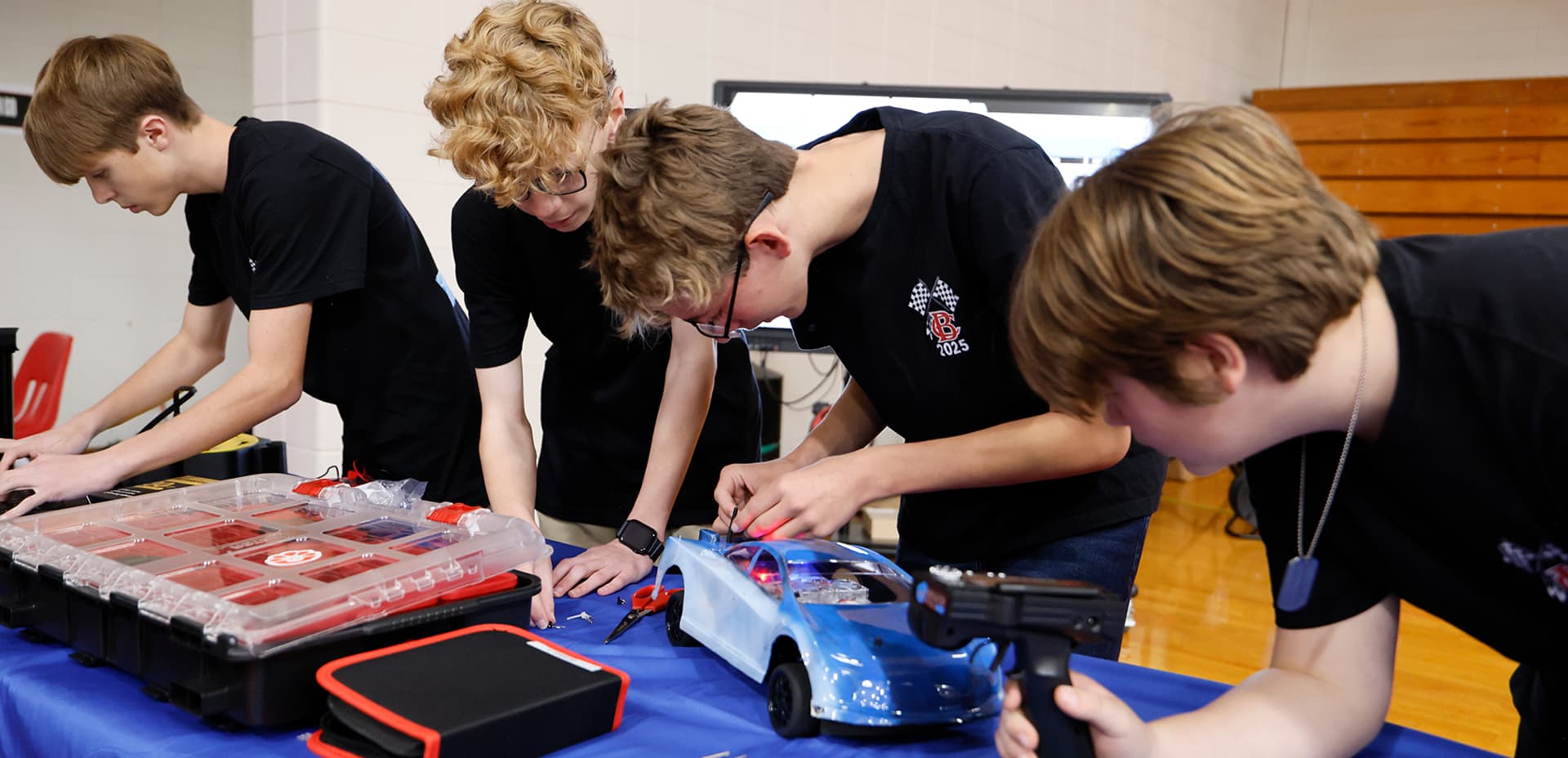 Four students in black shirts working together to assemble a remote control car at a table during a competition.